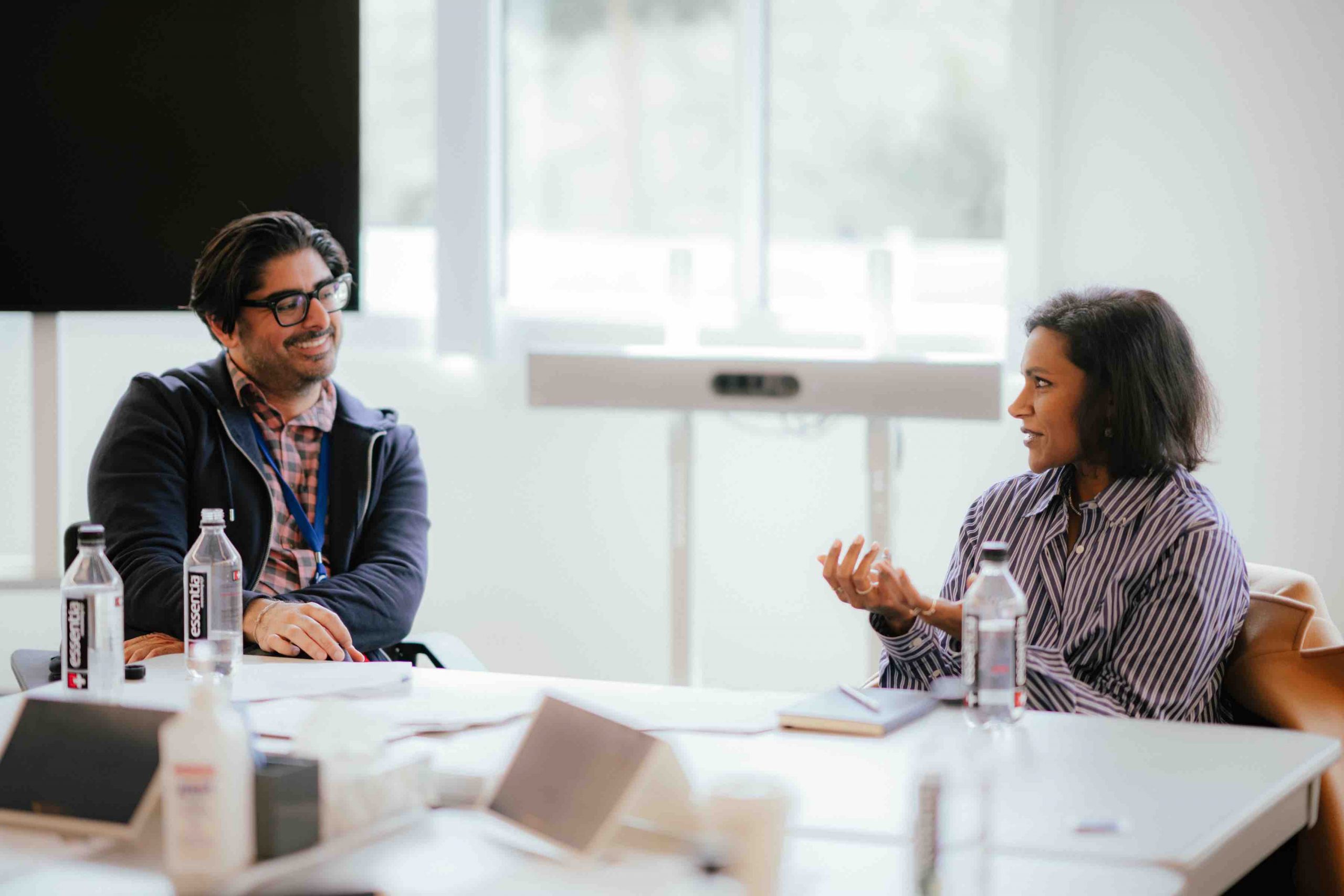 At the head of a conference table, Pillars President Kashif Shaikh smiles at Mindy Kaling who is speaking with her palms facing up