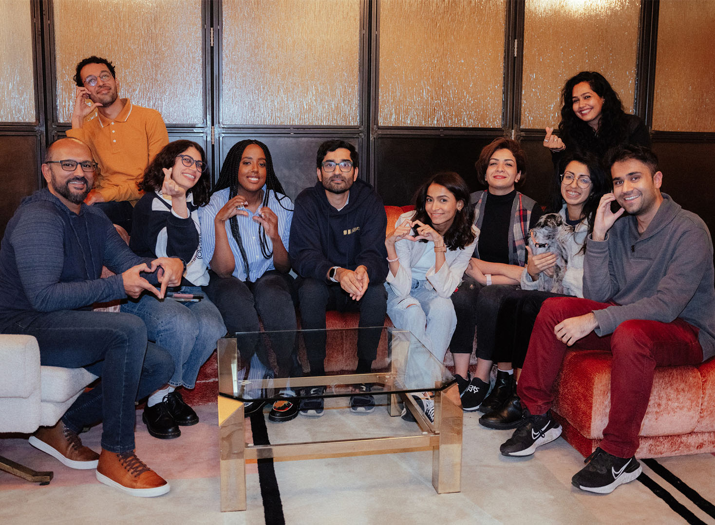 10 Pillars Artist Fellows sitting on chairs making heart signs with their hands