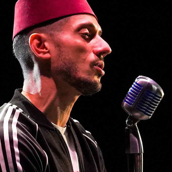 Omar Offendum wearing a red fez singing into a microphone