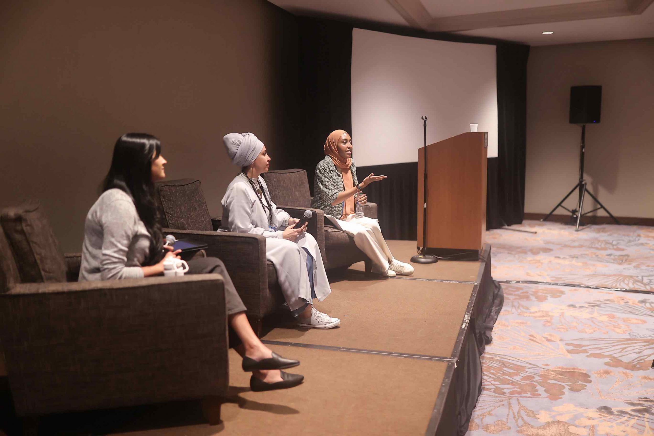 Georgia Muslim Voter Projects' Hibah Berhanu, Project South's Juilee Shivalkar, and Maha ELKolalli sit in armchairs on a stage with handheld microphones in hand.