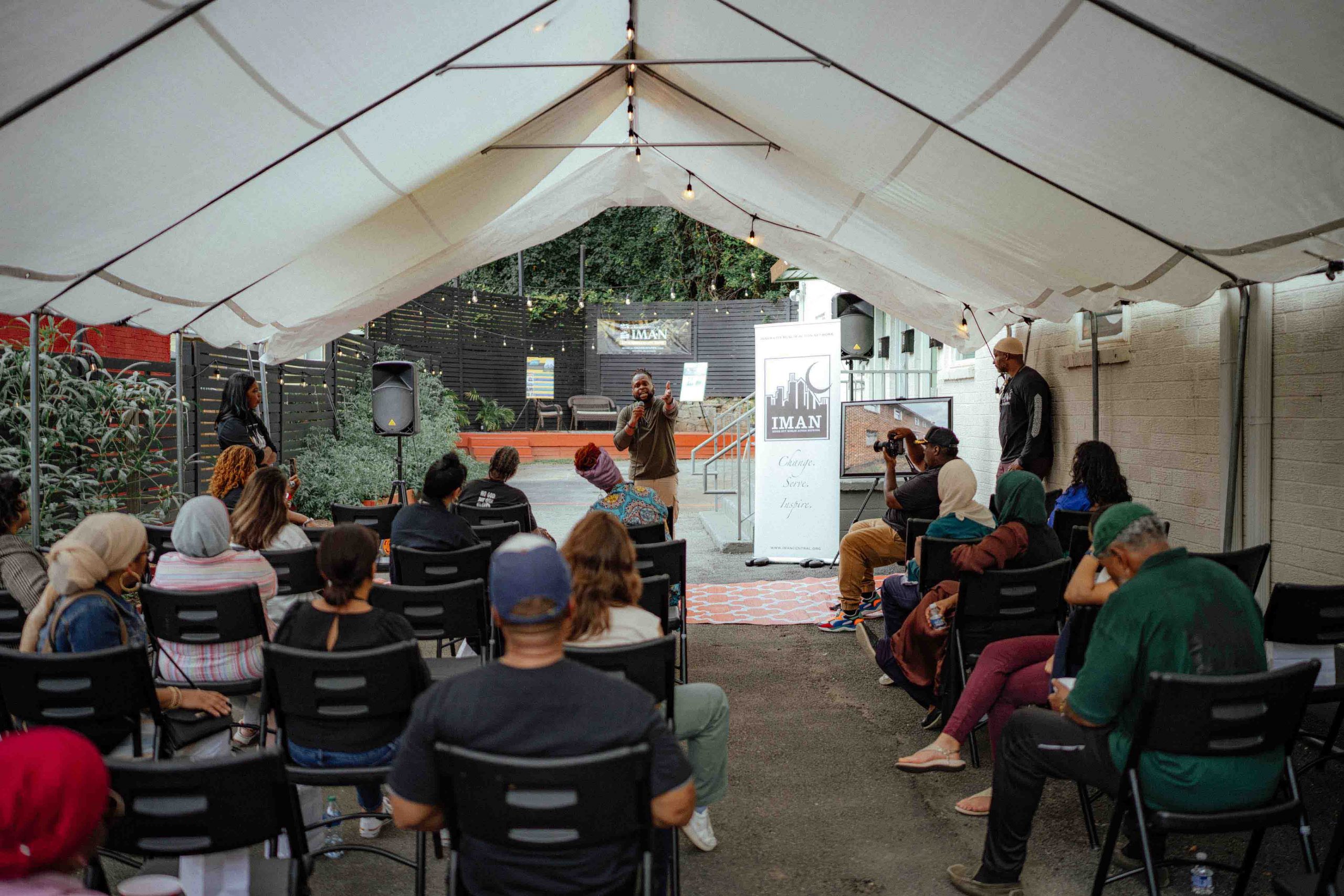 Our Pillars group of staff and grantee partners sits in a white tent listening to an IMAN Atlanta poetry performance