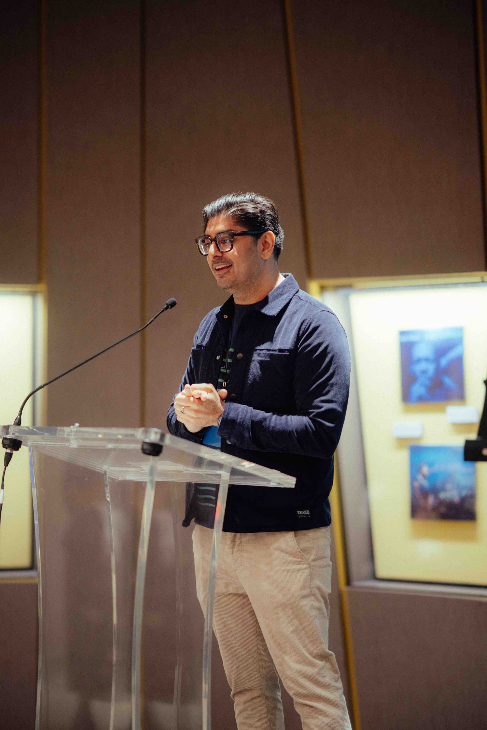 Pillars President and Cofounder Kashif Shaikh stands in front of a podium, speaks into a microphone, and clasps his hands together