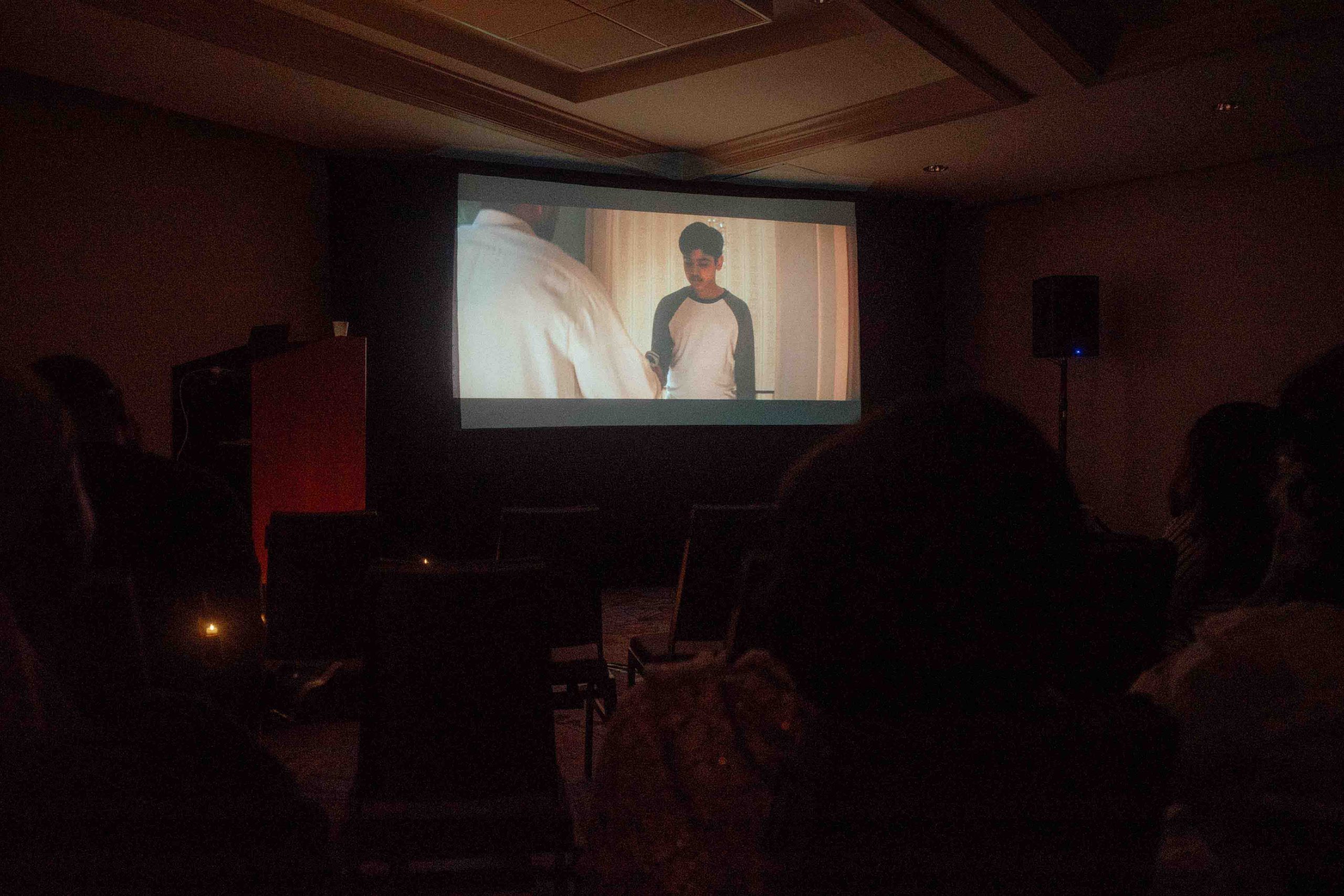 A projector screen in a dark conference room shows a scene from the film 