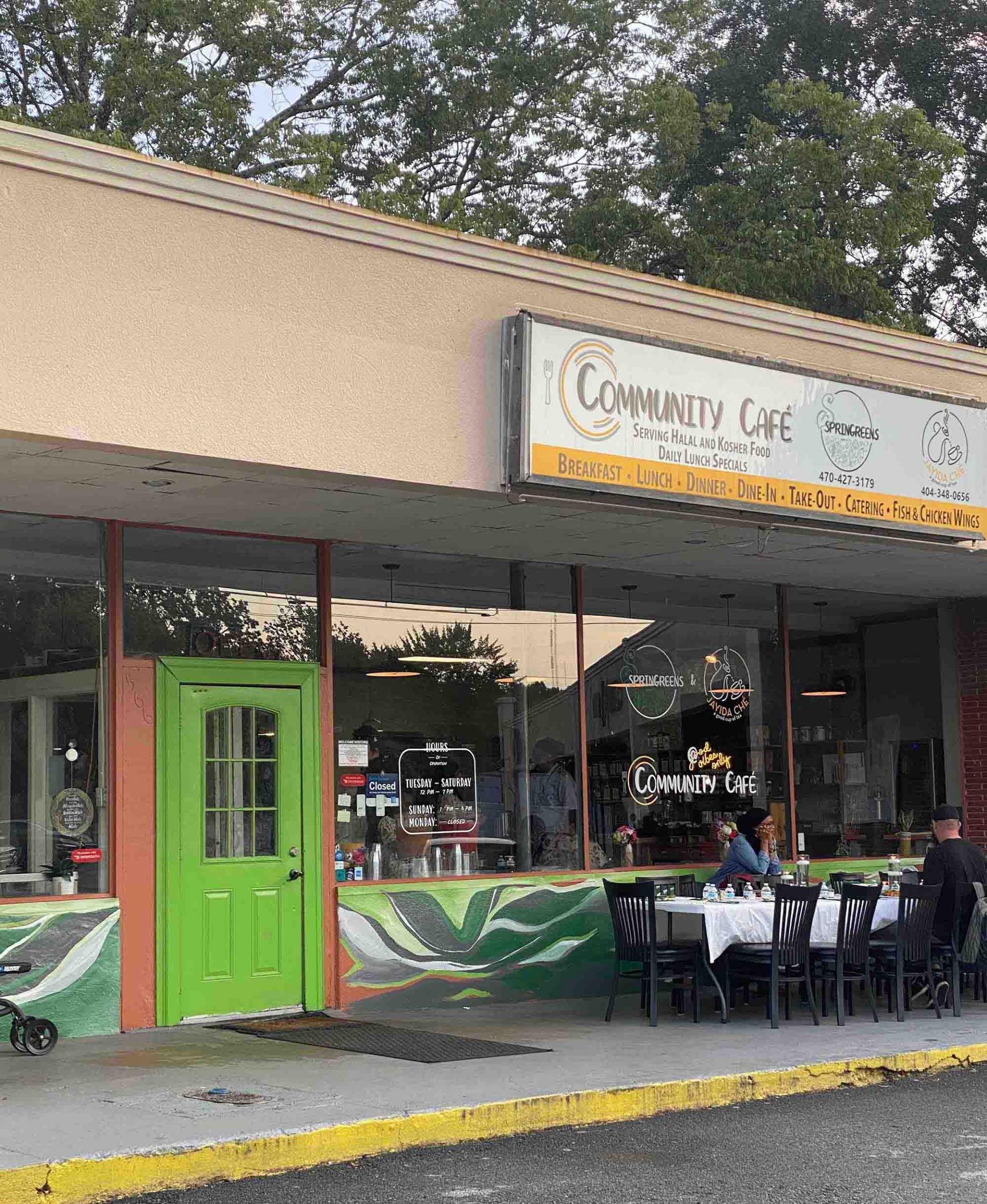 The front of Springreens at Community Cafe, with a bright green door and a table out front for diners to sit and enjoy.
