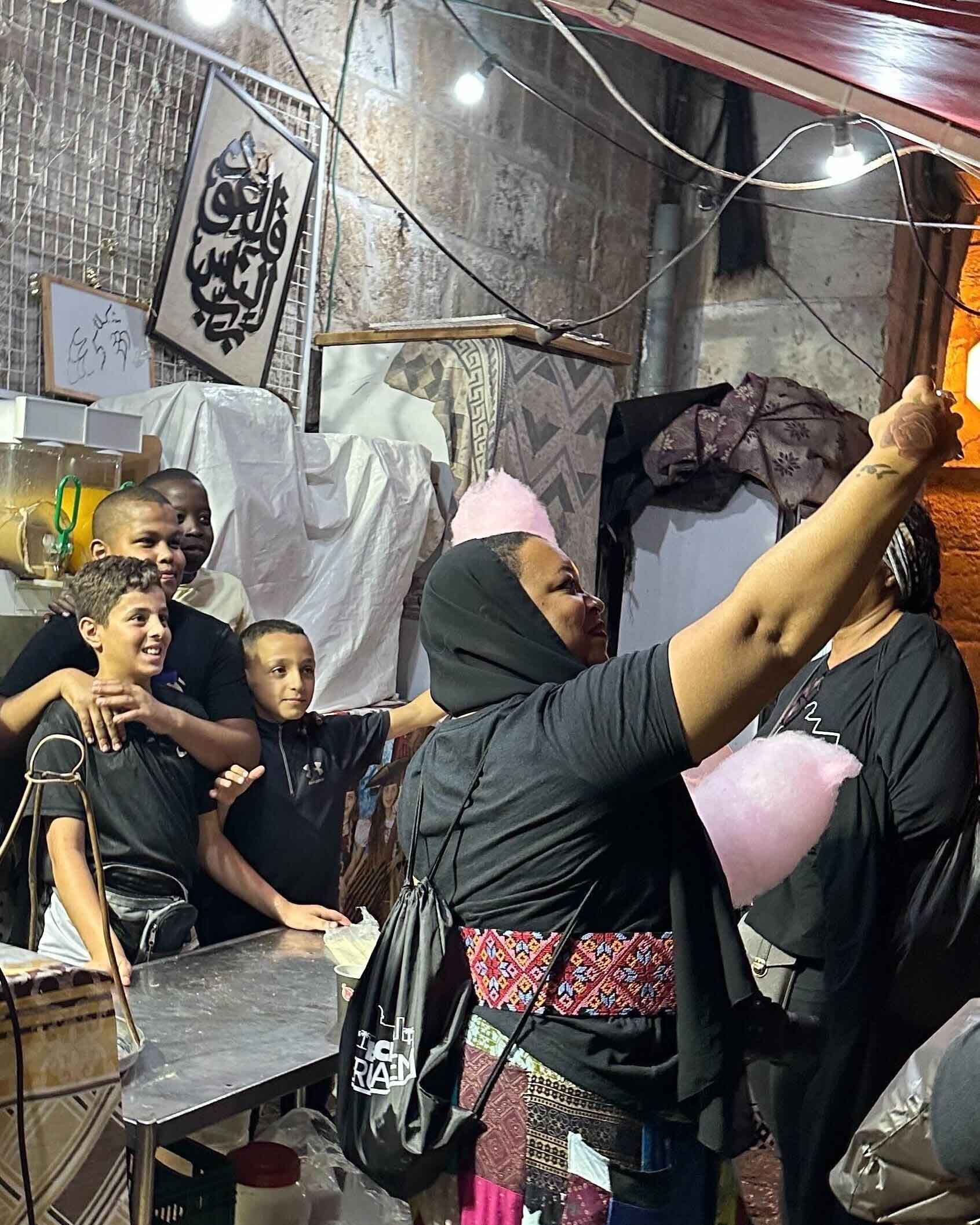A photo of a joyful woman holding up her phone, capturing a selfie moment with a group of smiling Palestinian kids in the background.